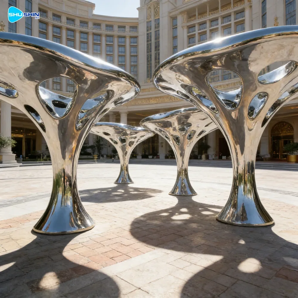 Large mirror-polished stainless steel abstract sculpture installed in a hotel courtyard plaza with classical European architecture and manicured garden